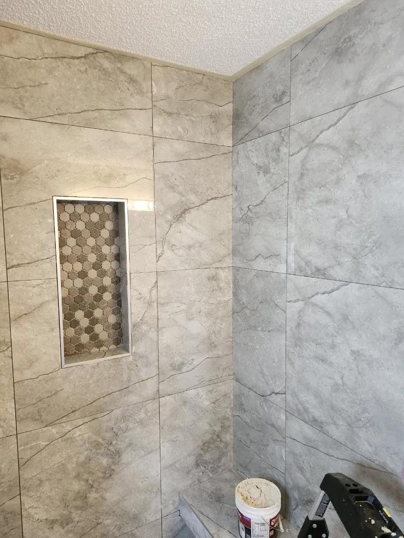 Grey marble-look tile shower with mosaic niche mid-installation by BBJ Flooring Corp