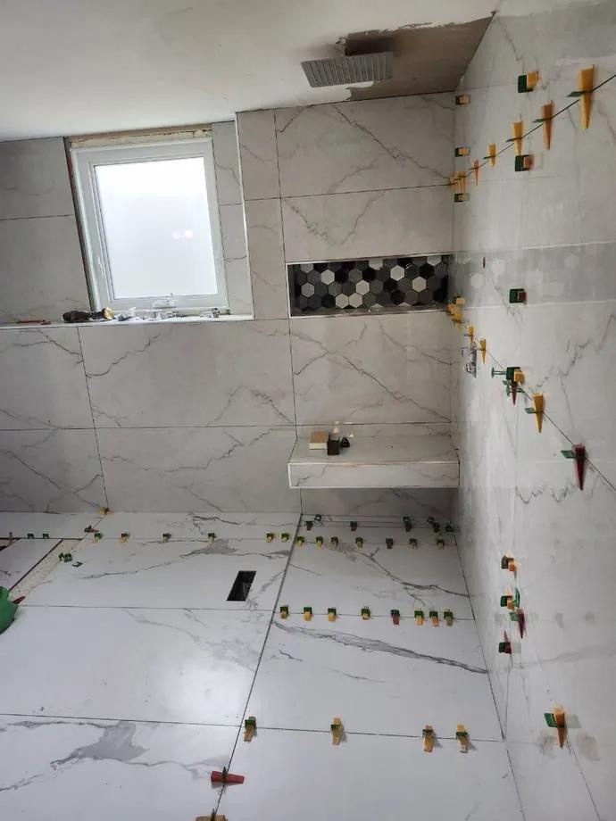 Marble-look tile shower with hexagon mosaic niche mid-installation by BBJ Flooring Corp