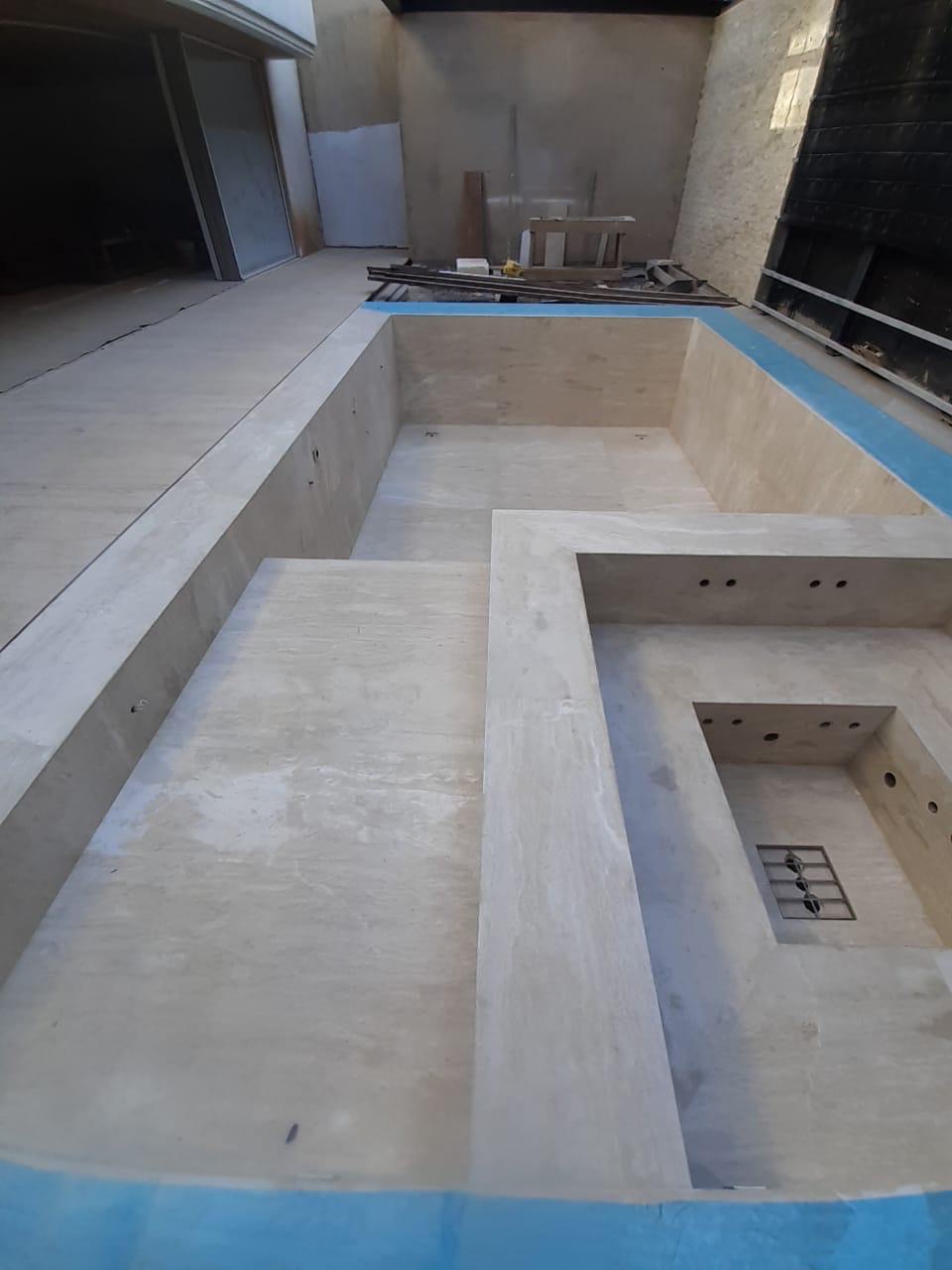 Outdoor pool with integrated spa lined in travertine-look tile mid-installation by BBJ Flooring Corp