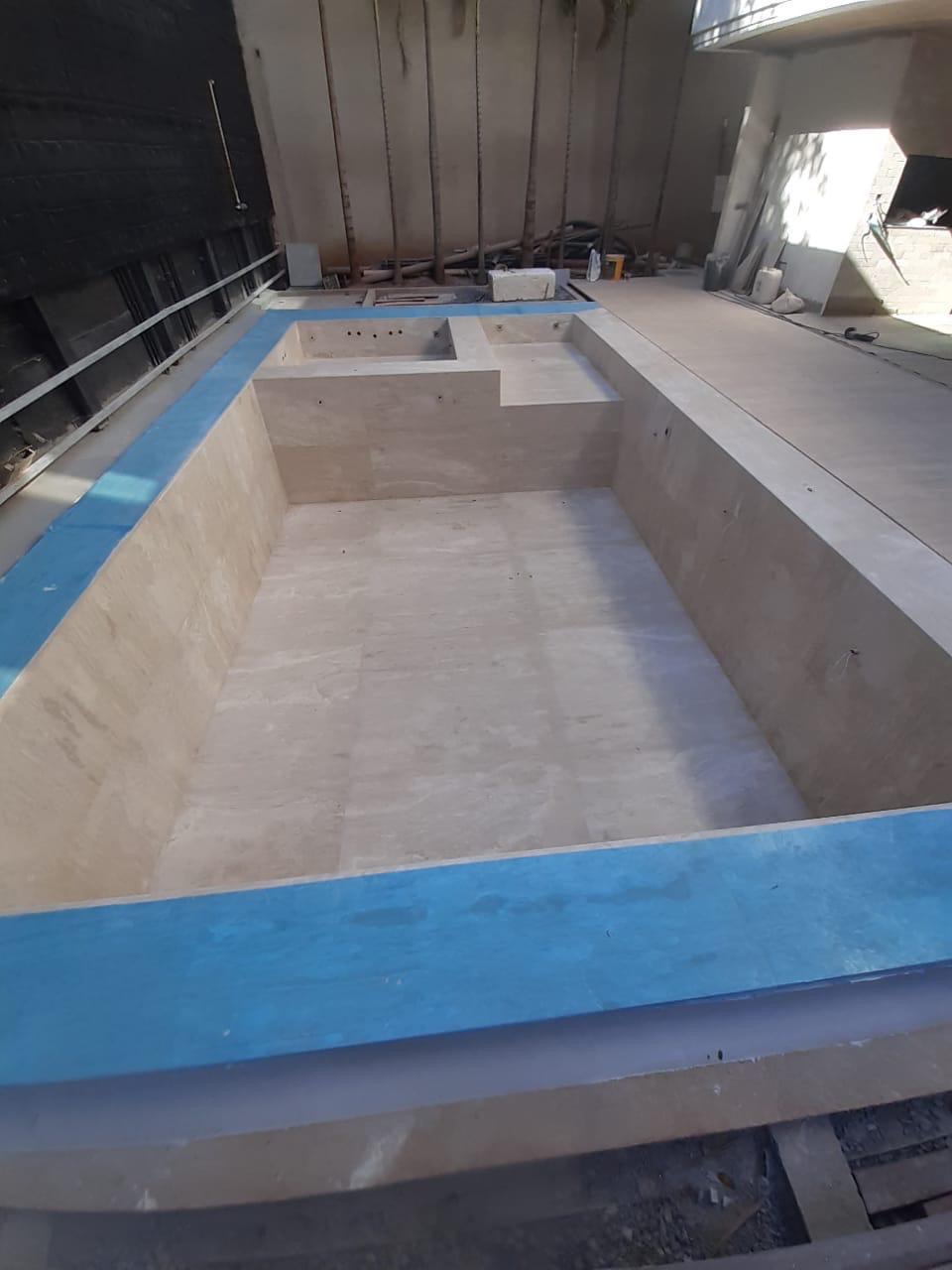 Outdoor pool with integrated spa lined in travertine-look tile mid-installation by BBJ Flooring Corp