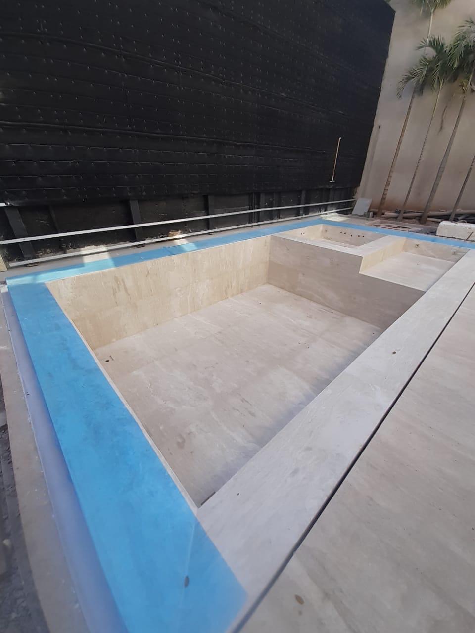 Outdoor pool lined with travertine-look tile mid-installation by BBJ Flooring Corp