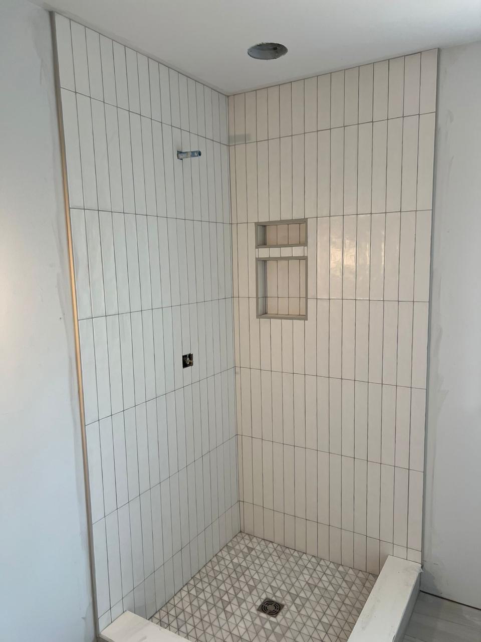 Vertical tile shower with mosaic tile floor mid-installation by BBJ Flooring Corp